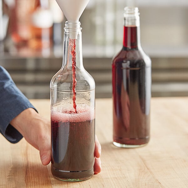 A person pouring red liquid into a glass bottle.