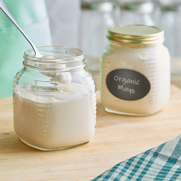 A square glass jar of white liquid with a label on the table next to a spoon.