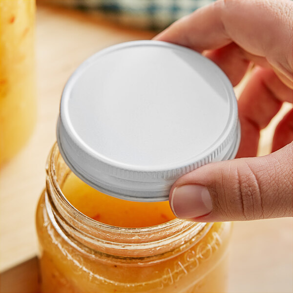 A hand holding a jar with a 70/450 white metal lid on it.