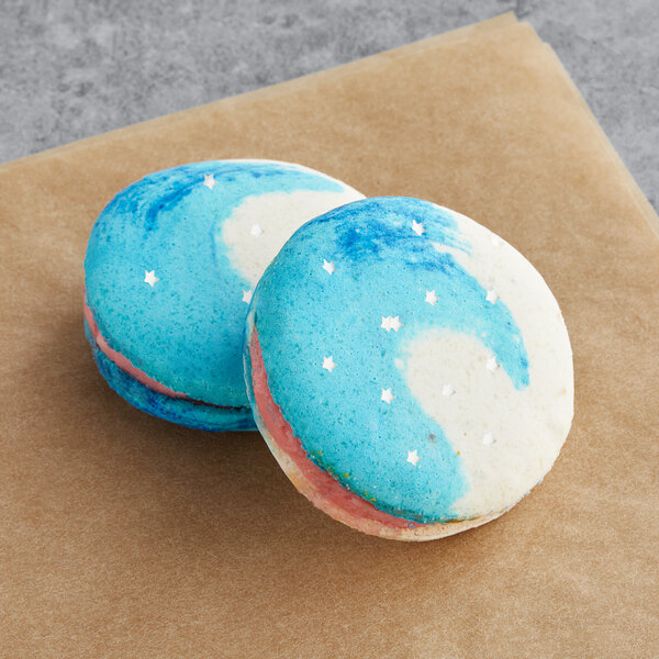 Two blue and white Macaron Centrale macarons with white stars on a brown surface.