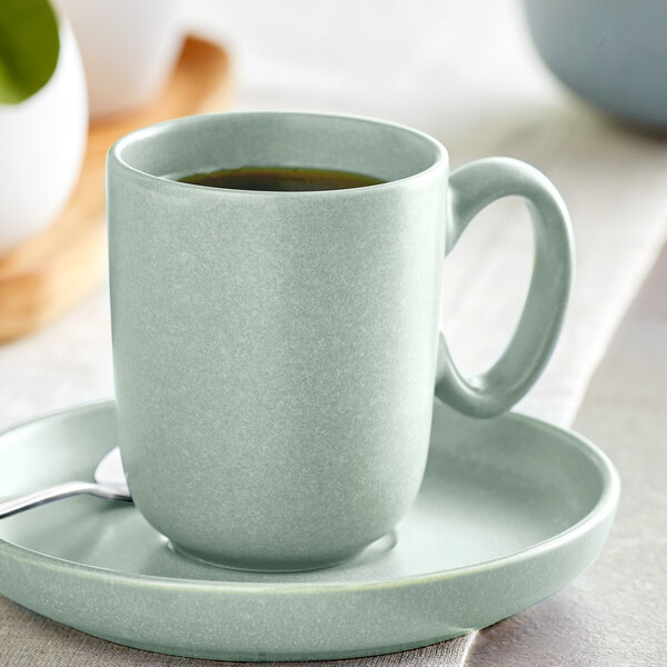 A Harbor Blue Acopa Pangea porcelain cup and saucer with a spoon on a table.