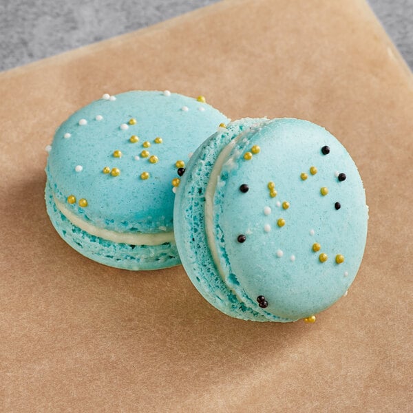 Two blue Macaron Centrale macarons with white and black sprinkles.