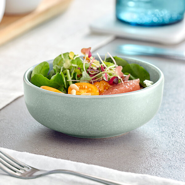An Acopa Pangea Harbor Blue Nappie Bowl filled with salad with greens, tomatoes, and fruit.