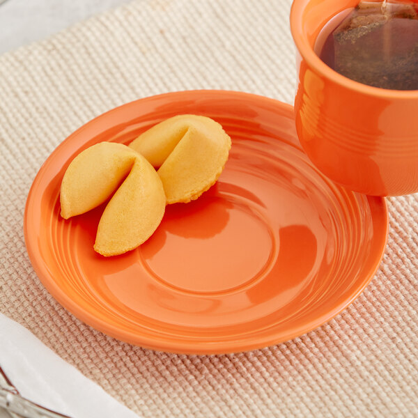 An Acopa Capri Valencia orange stoneware saucer with a cup of tea on it.
