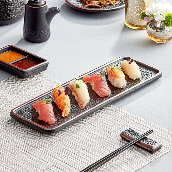 A black rectangular Acopa stoneware plate with sushi on it.