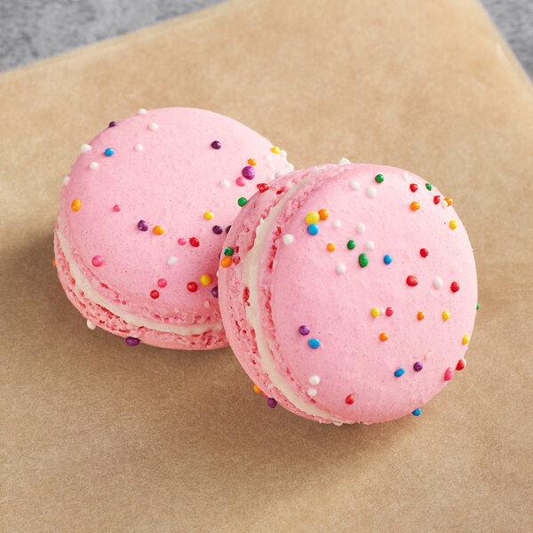 Two pink Macaron Centrale macarons with sprinkles on top on a brown paper.