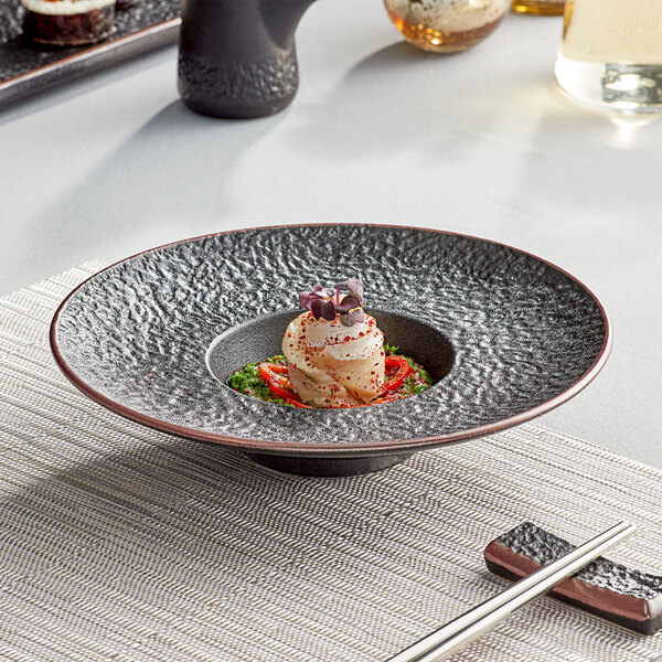 A black Acopa stoneware bowl with food and chopsticks on a table.