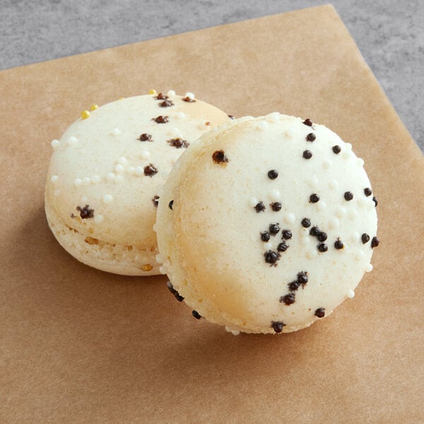 A white Macaron with black specks and a brown Macaron with white specks on top of brown paper.