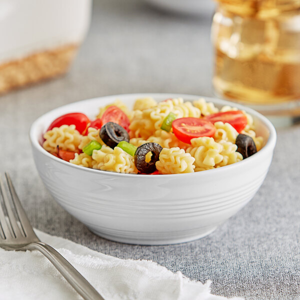 An Acopa Capri coconut white stoneware bowl filled with pasta, tomatoes, and olives on a napkin with a fork.