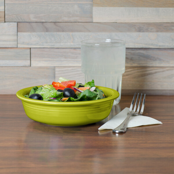 A lemongrass Fiesta china bowl filled with salad on a table with a glass of water.