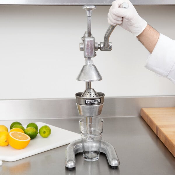 A person wearing gloves uses a Nemco Manual citrus juicer to squeeze lemon juice into a glass.