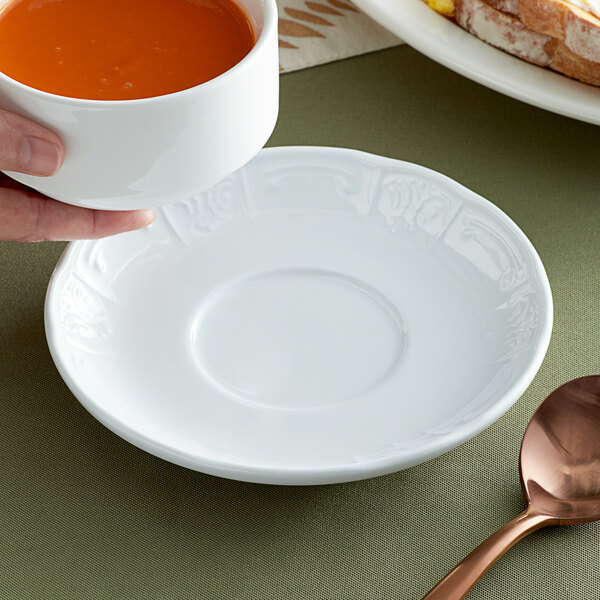 A person holding a Tuxton bright white soup mug over a white saucer.