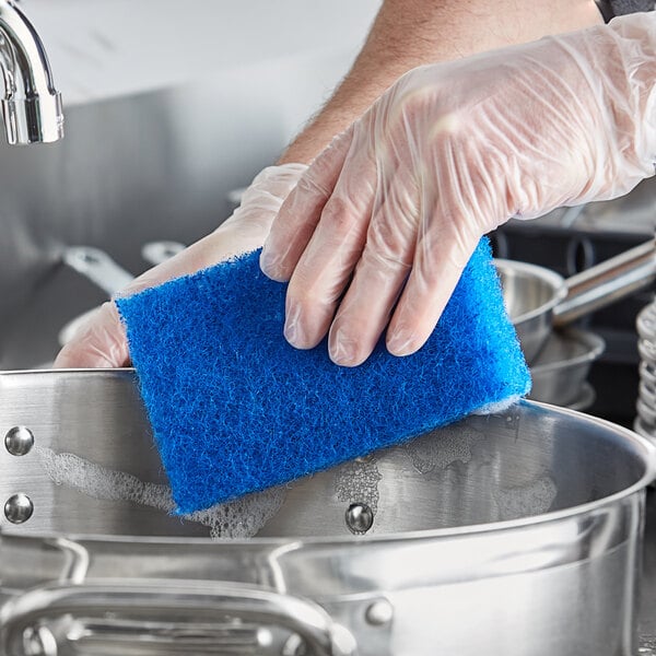 A person in gloves scrubbing a pot with a Lavex blue sponge.