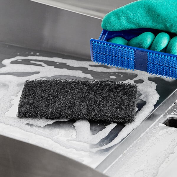 A hand in a glove using a sponge to clean a metal sink.
