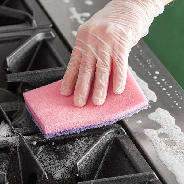 A hand in a plastic glove using a pink sponge to clean a counter.