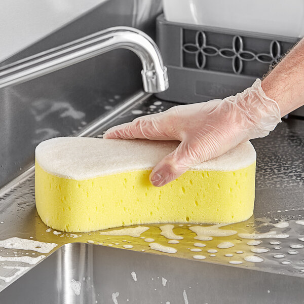 A person's gloved hand scrubbing a yellow Lavex sponge.