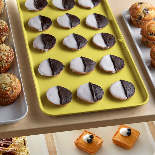 A yellow Cambro market tray on a counter with cookies, muffins, and pastries.