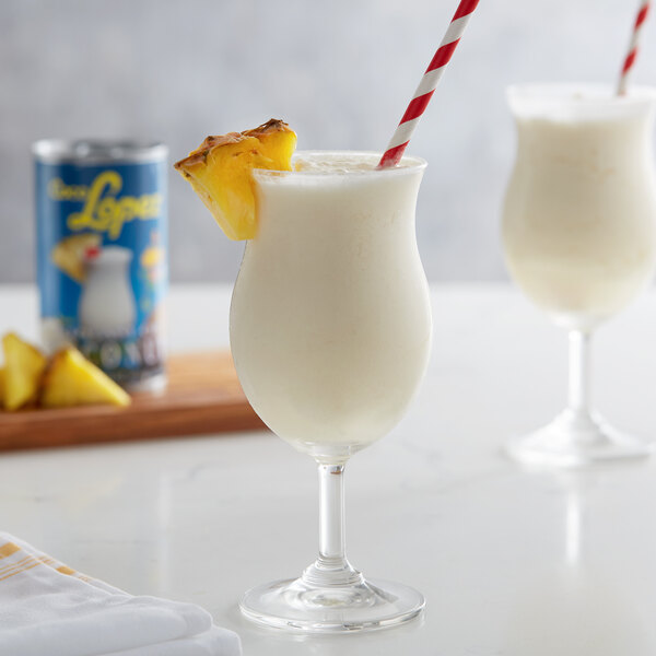 A glass of white liquid with a straw and pineapple slice on top.
