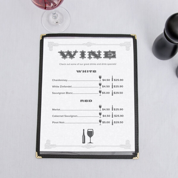 A black menu with a scroll border on a table with a glass of wine.