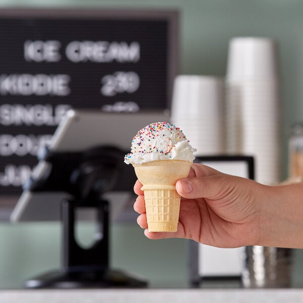 A hand holding a JOY flat bottom ice cream cone in front of a counter.