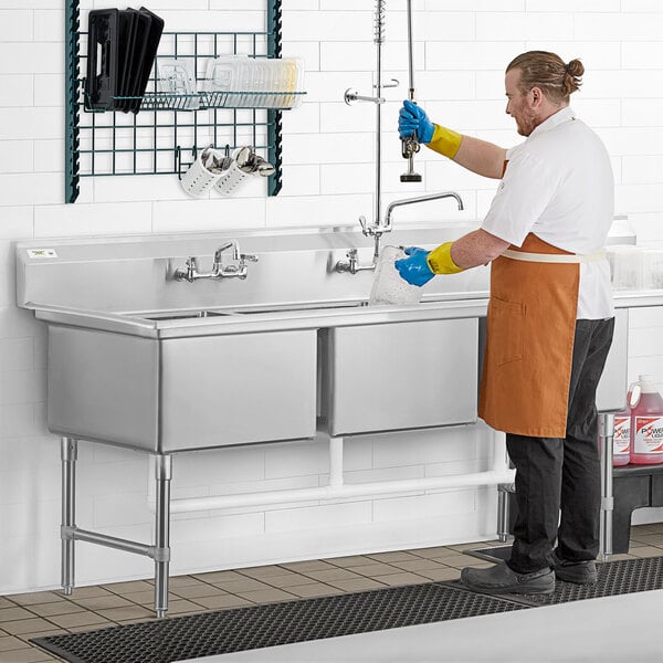 A man in an apron and gloves washing a Regency three compartment sink with a drainboard.