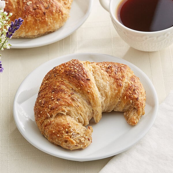 A Bridor multigrain croissant on a plate with a cup of coffee.