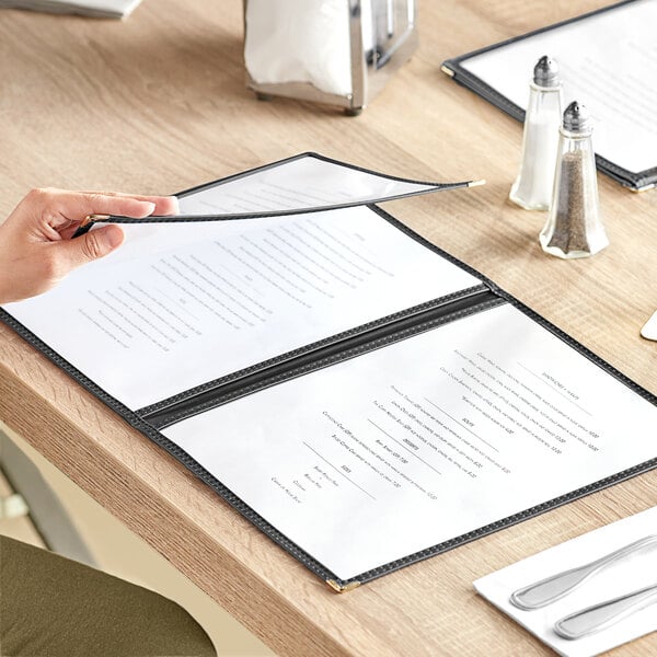 A hand opening a Choice black 6-view trifold menu on a table with salt and pepper shakers.