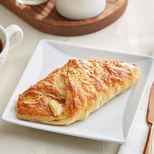 A Bridor almondine danish on a plate with a cup of coffee.