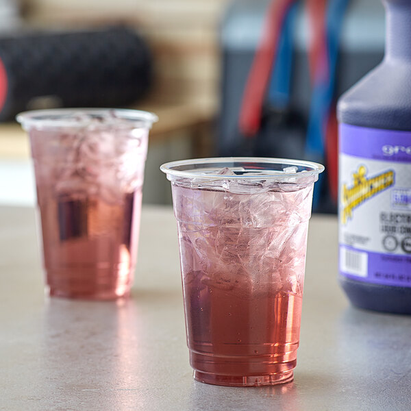 Plastic cups filled with pink Sqwincher grape beverage on a table.