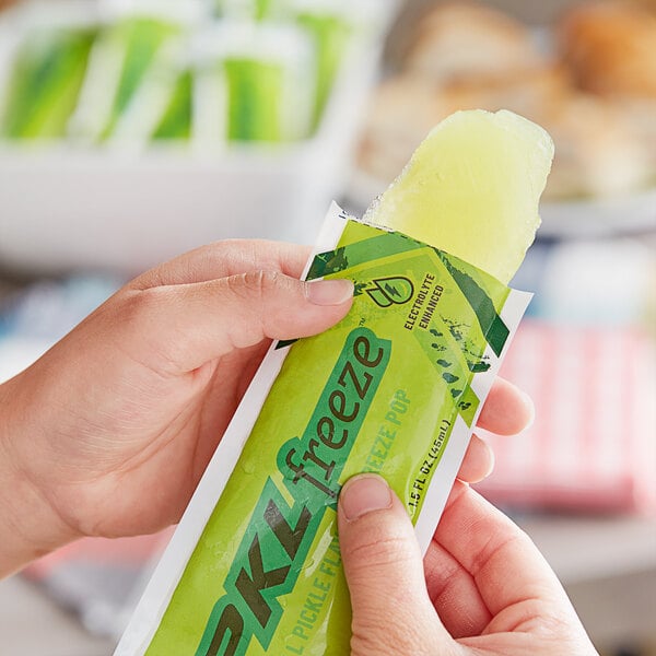 A person holding a PKL Freeze Dill Pickle freezer pop with a yellow and green wrapper.