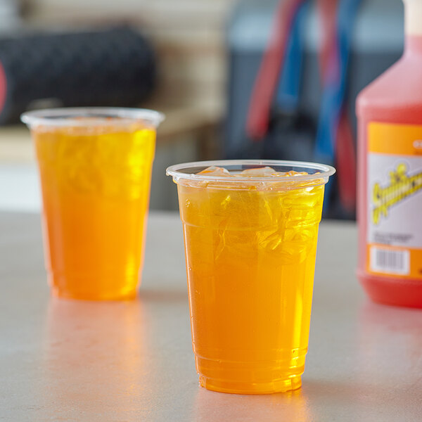 Two plastic cups of Sqwincher orange liquid on a counter.