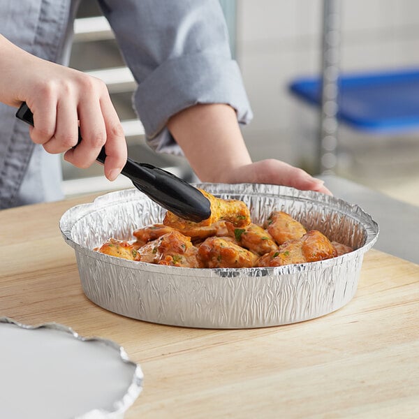 A person using a spatula to put food in a Choice foil take-out pan.