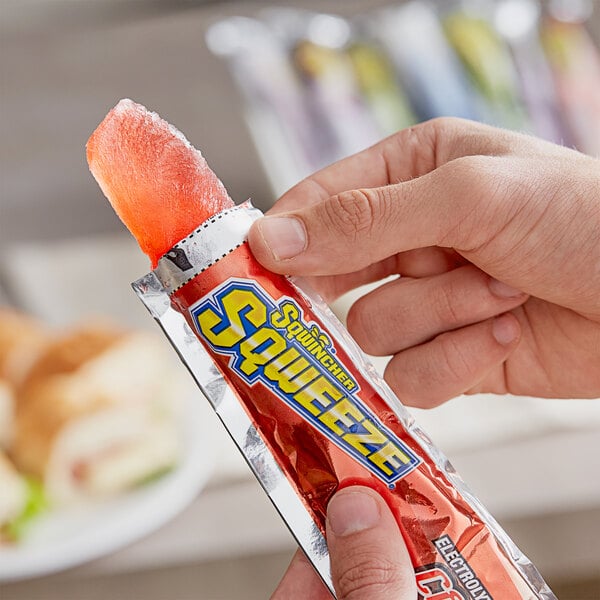 A hand holding a red Sqwincher electrolyte freezer pop.