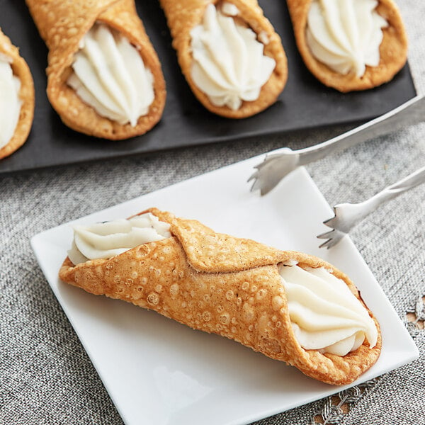 A plate with Brooklyn Cannoli shells filled with cream on a white background.