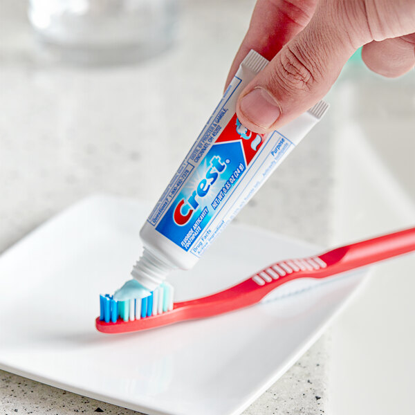 A hand holding a tube of Crest toothpaste and putting it on a toothbrush.
