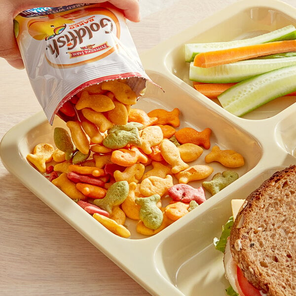 A hand pouring a bag of Pepperidge Farm Whole Grain Colors Goldfish crackers onto a tray of food.