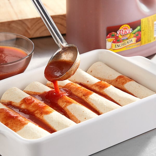 A white dish of enchiladas being spooned with red Pace Enchilada Sauce.