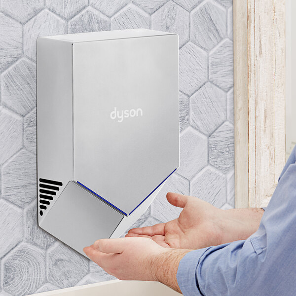 A person using a Dyson Nickel Airblade V hand dryer to dry their hands.