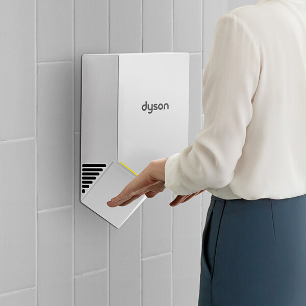 A woman using a white Dyson Airblade V hand dryer.