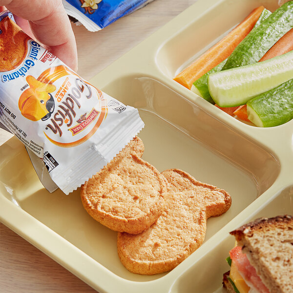 A hand putting a Pepperidge Farm Giant Vanilla Goldfish Graham packet into a tray of food.