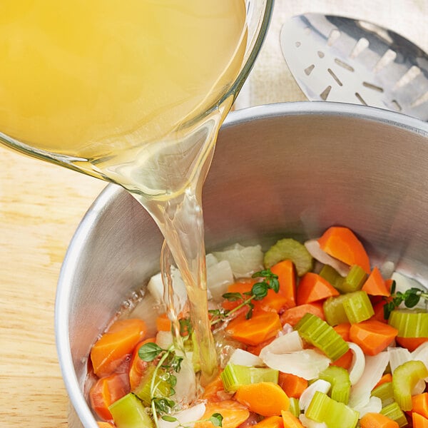 Swanson Chicken Broth being poured into a bowl of vegetable soup.