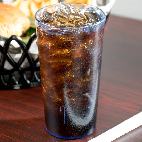 A Cambro slate blue plastic tumbler filled with soda and ice on a table with a burger in the background.
