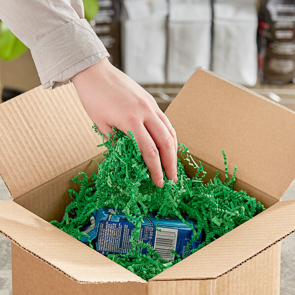A hand holding Spring-Fill green crinkle cut paper in a cardboard box.