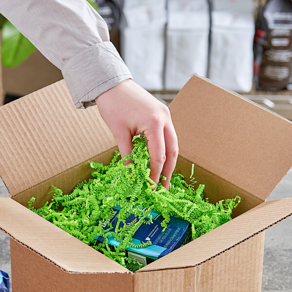 A hand reaching out to a cardboard box filled with Spring-Fill lime green paper shred.