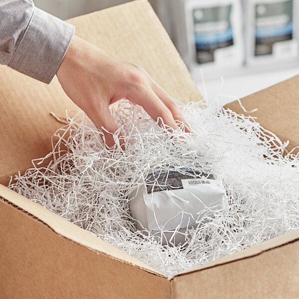 A hand putting Spring-Fill Very Fine white shredded paper into a cardboard box.