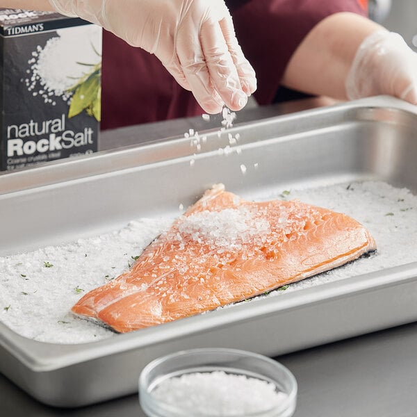 A person sprinkling Tidman's Natural Rock Salt on a piece of salmon.