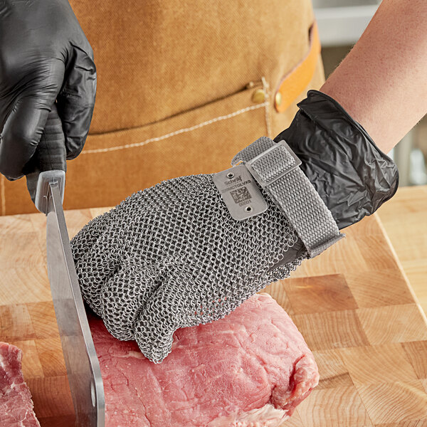 A person wearing a Schraf stainless steel mesh glove cutting meat with a knife.