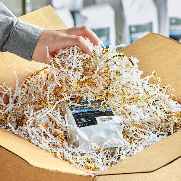 A hand holding a package of coffee beans in a box filled with Spring-Fill gold and white shredded paper.