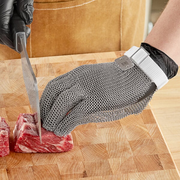 A person wearing Schraf stainless steel mesh gloves cutting meat with a knife.
