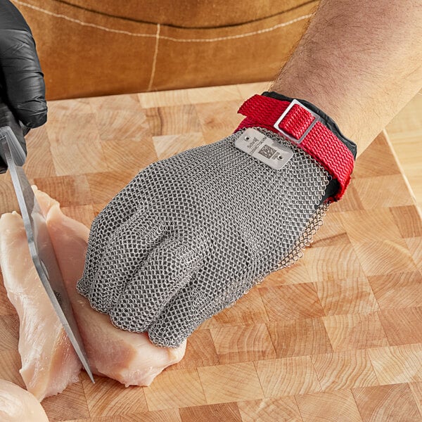 A person wearing Schraf stainless steel mesh gloves cutting meat with a knife.
